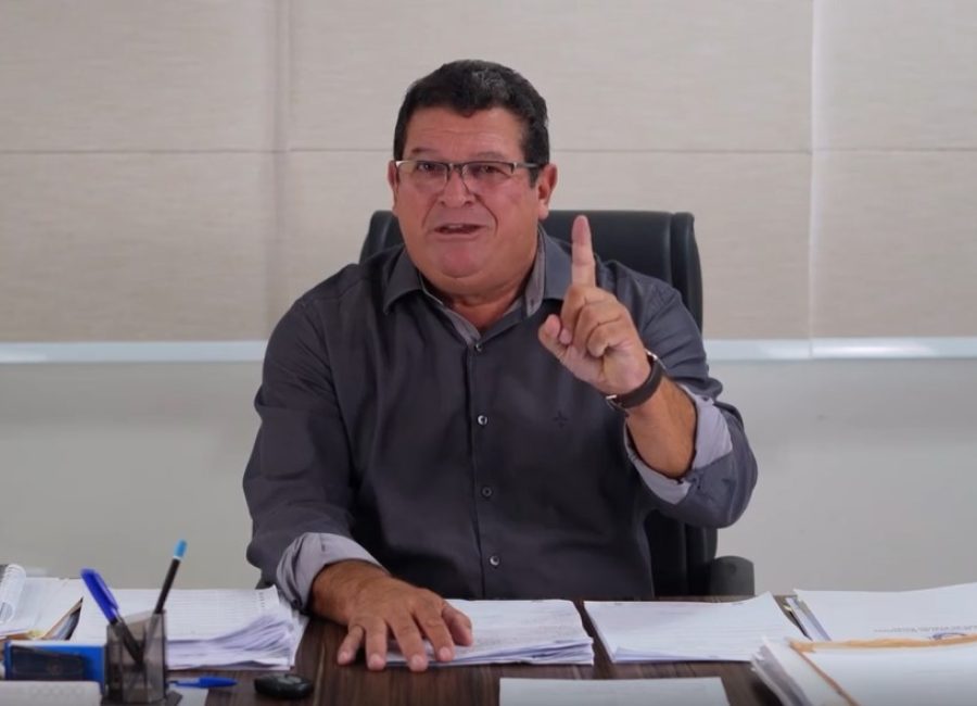 O ex-prefeito de Marataízes, Tininho Batista, de óculos e camisa cinza, sentado à mesa de escritório, gesticula e levanta o dedo indicador em sinal de afirmação.